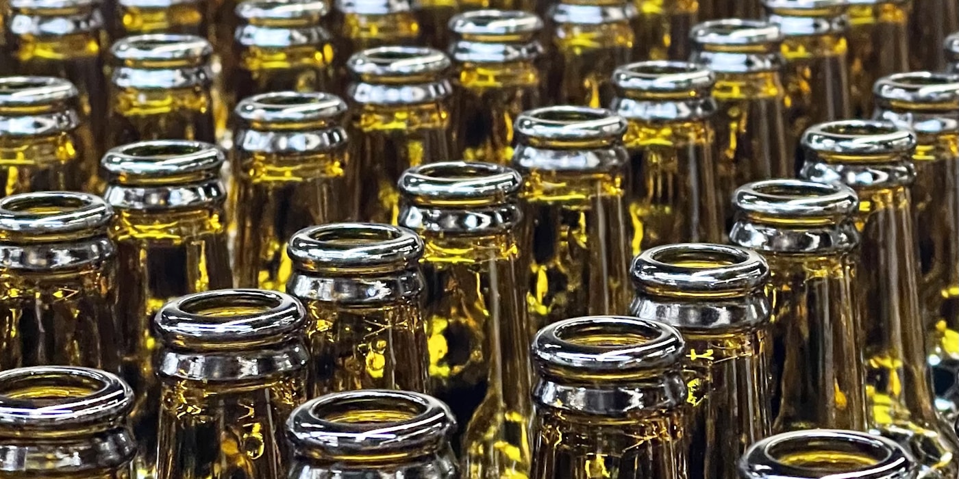 Rows of empty amber glass bottles seen close up at the crown finish