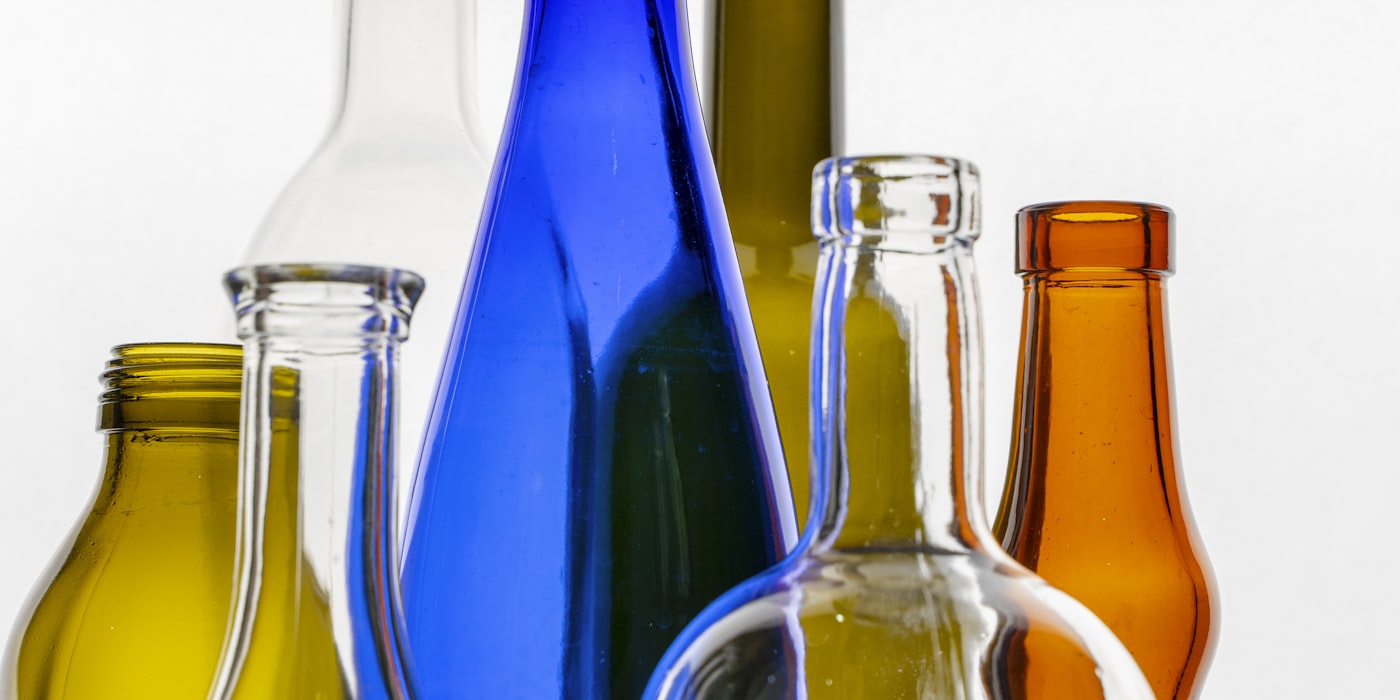 Leere Glasflaschen in Braun, Blau, Grün und Klar nebeneinander vor hellem Hintergrund