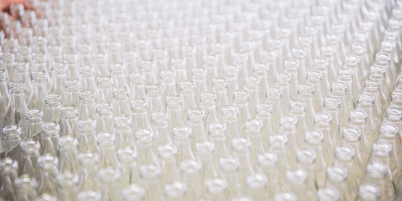 Rows of empty clear glass bottles with threaded finishes stacked on a pallet
