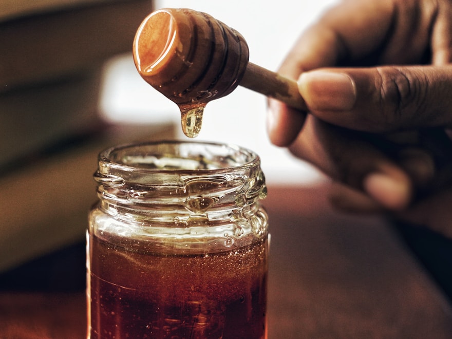 Honey lifted from a glass honey jar with a wooden dipper