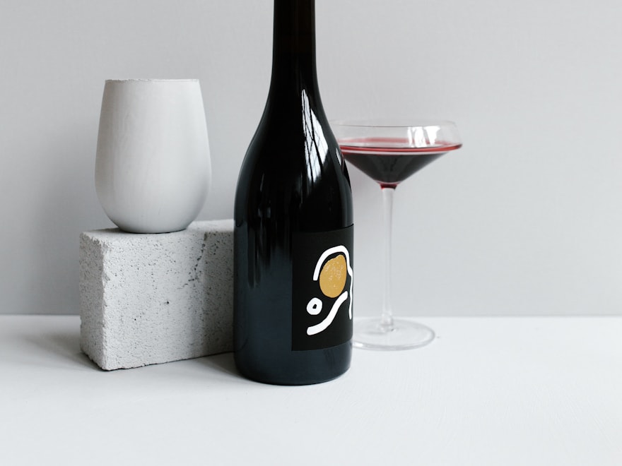 Dark glass wine bottle beside a filled glass on a light surface
