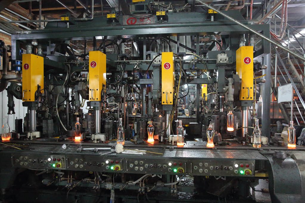 Hot glass bottles on the forming section of an IS machine at the Shandong factory