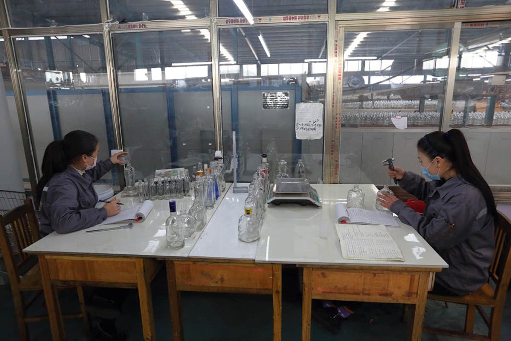 Quality control lab technicians inspecting and measuring glass bottles