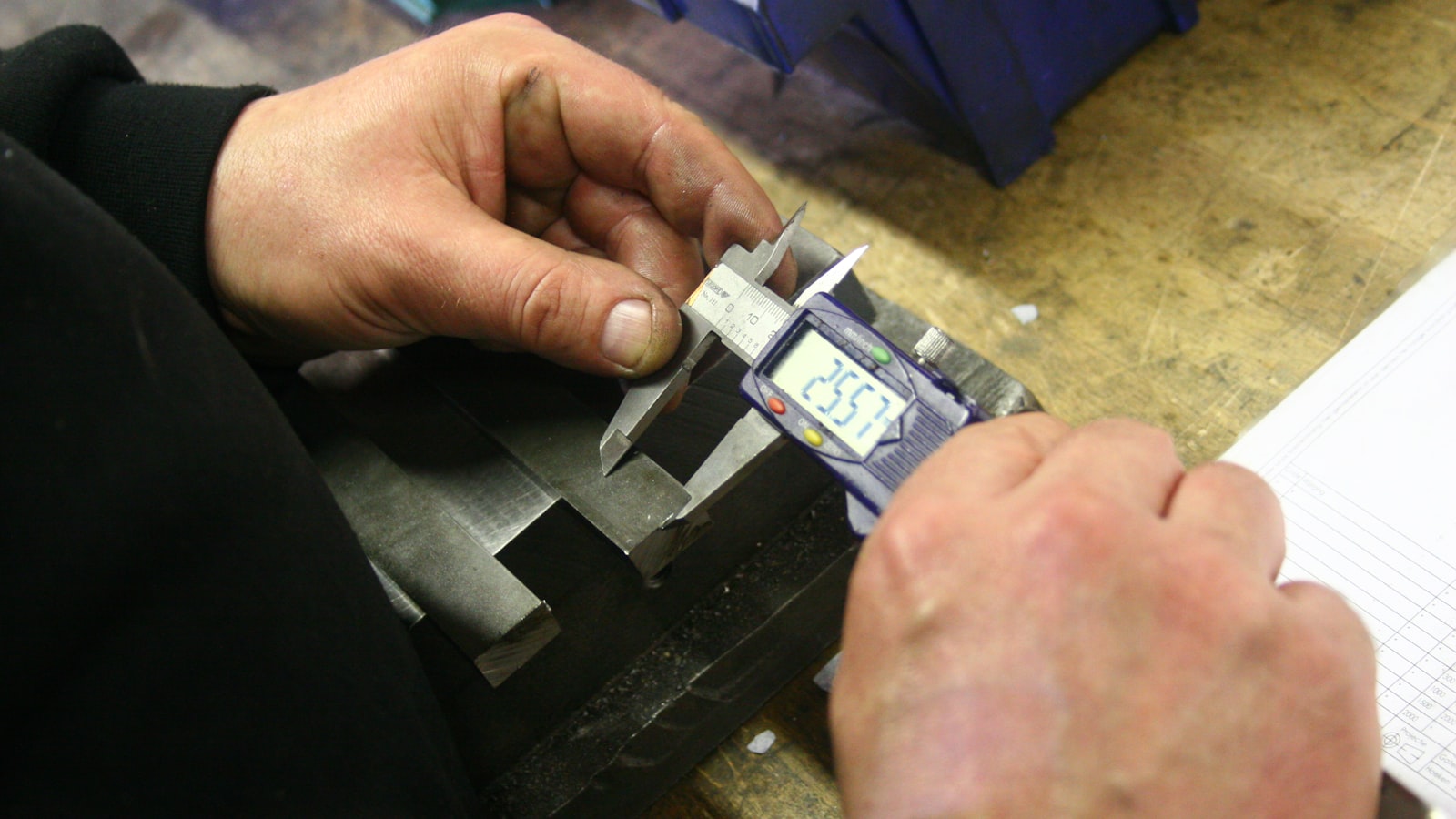 A caliper measuring a machined metal part on a bench