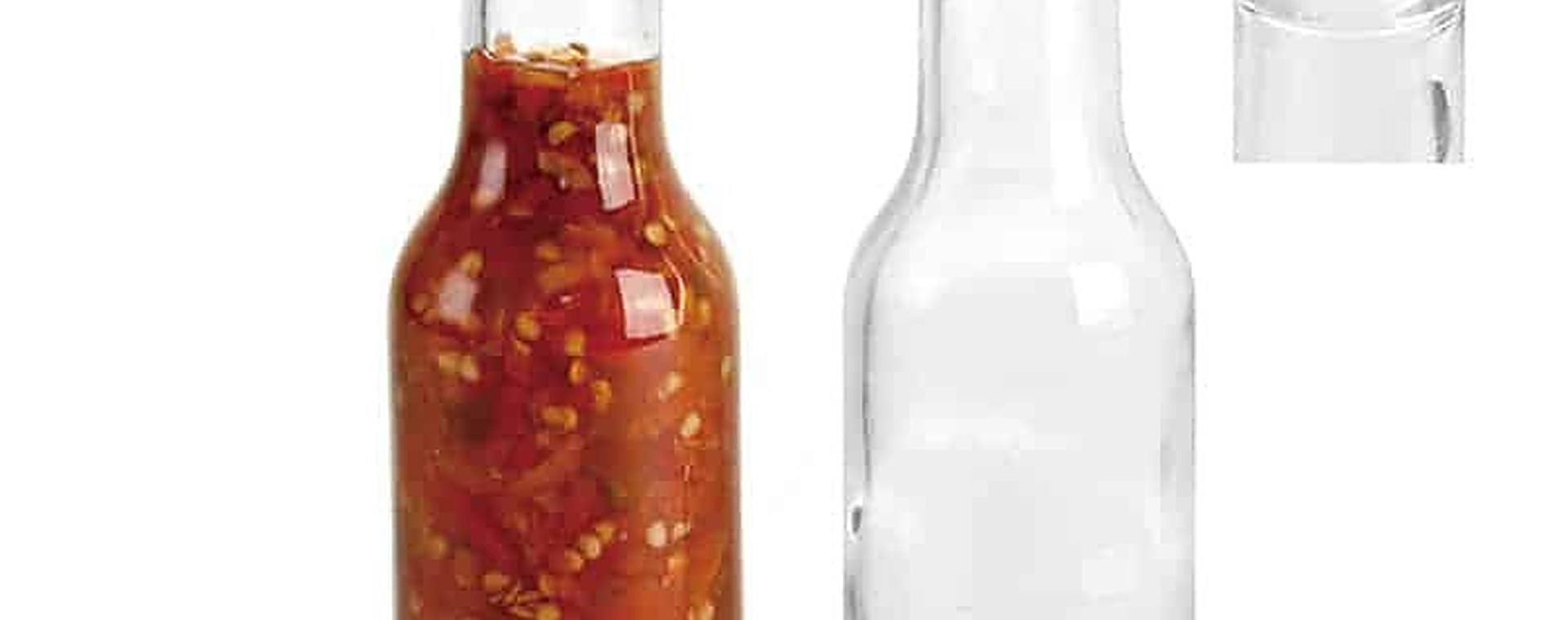 Klare Woozy-Flasche neben einer mit roter Sauce gefüllten Flasche, einem Dosiereinsatz und einem Verschluss