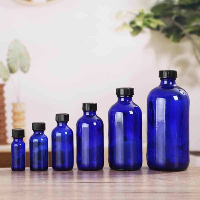 Frascos Boston azul cobalto con tapaderas negras y atomizadores sobre una superficie de madera
