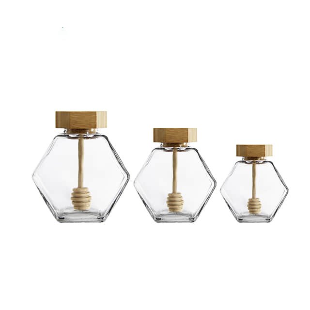 Drei leere Sechskant-Honigtöpfe aus Glas mit Holzdeckeln und Honigheber