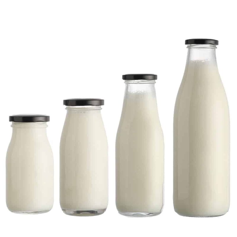 Cuatro botellas redondas clásicas de vidrio para leche en escalera de tamaños, llenas de leche, con tapa oscura a rosca