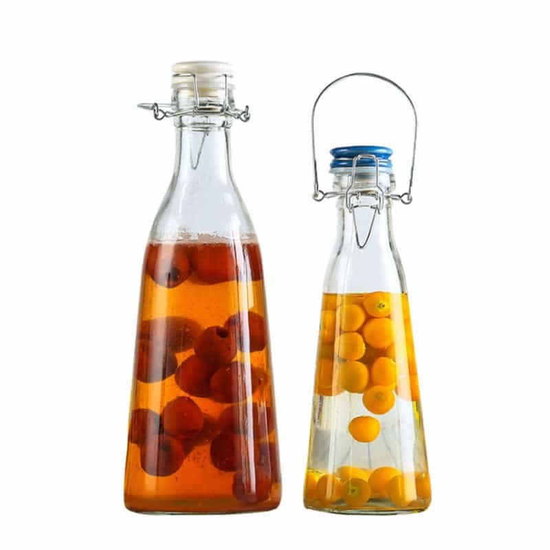 Dos botellas de vidrio con asa de alambre para llevar, llenas de té de frutas