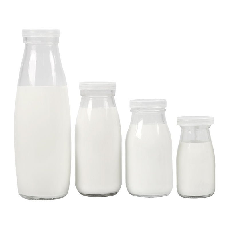 Cuatro botellas redondas de vidrio para leche con tapa blanca de plástico, llenas de leche