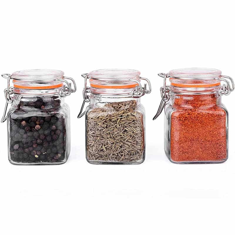 Tres tarros cuadrados de vidrio con tapa de clip para especias, llenos de pimienta en grano, comino y pimentón