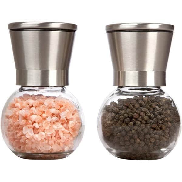 Dos molinillos de vidrio redondos y bajos con cabezal de acero inoxidable, llenos de sal en grano y pimienta en grano