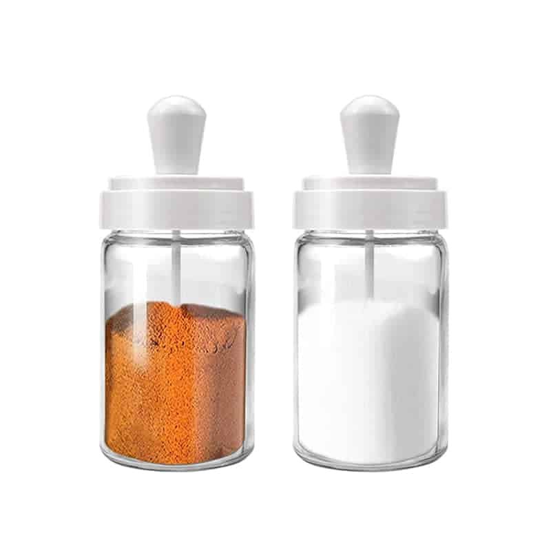 Tres tarros de vidrio transparente para especias con tapas que llevan una brocha, una cuchara y un cucharón
