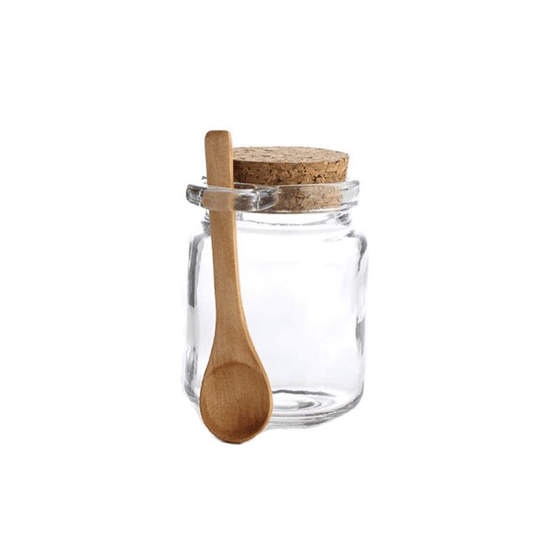 Tarro chico de vidrio transparente para especias con tapa de corcho y una cuchara de madera al lado