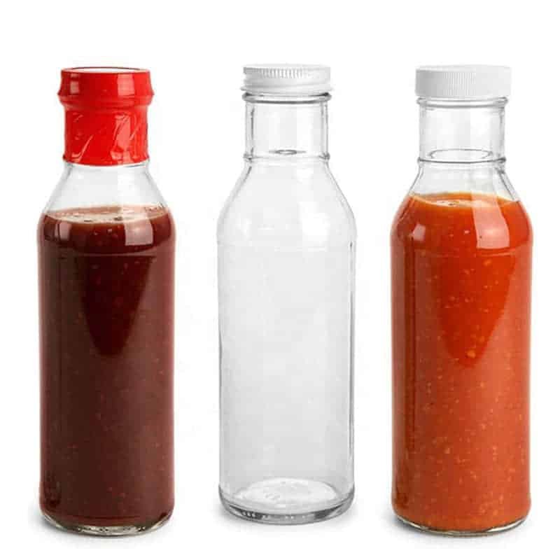 Gefüllte und leere Ringhals-Saucenflaschen in einer Reihe, zwei mit roter Sauce