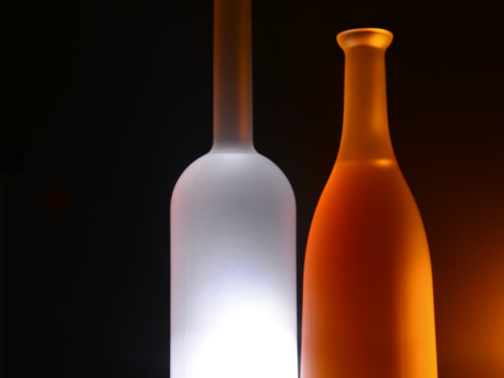 A frosted white and a spray-coated orange glass bottle lit from behind